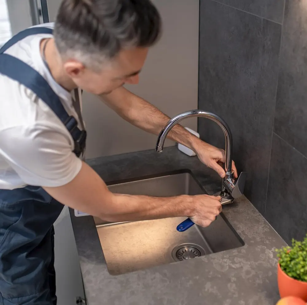 “A plumber fixing blocked kitchen sink tap, as part of a professional drain unblocking service in Jersey.
