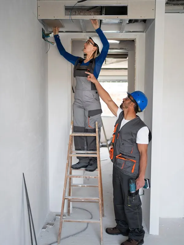 Two electricians installing electrical wiring in a ceiling in Jersey, representing expert electrical installation services.