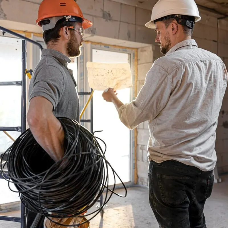 Two electrical installation experts in hard hats reviewing wiring plans at a Jersey construction site.