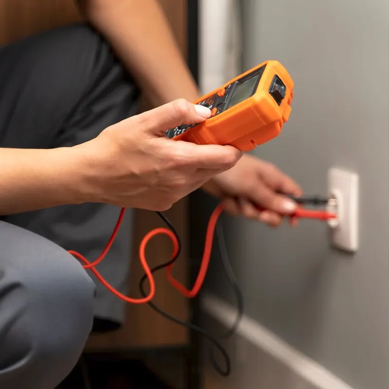 Close-up of a Jersey electrician using a digital multimeter to test an electrical socket.