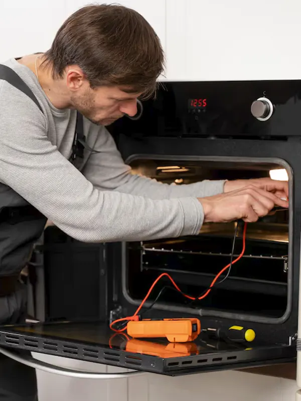 An appliance technician inspecting and repairing a built-in oven using a multimeter in Jersey.