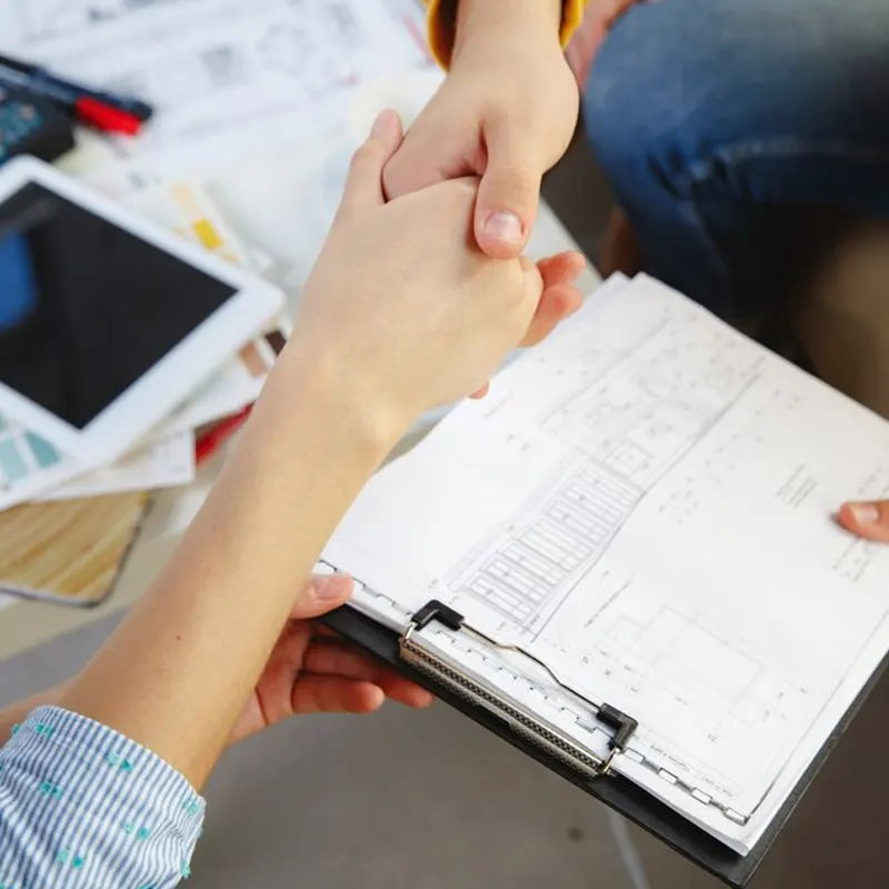 Two professionals shaking hands over electrical schematics, symbolising a successful agreement for an Electrical Installation Condition Report (EICR) in Jersey.