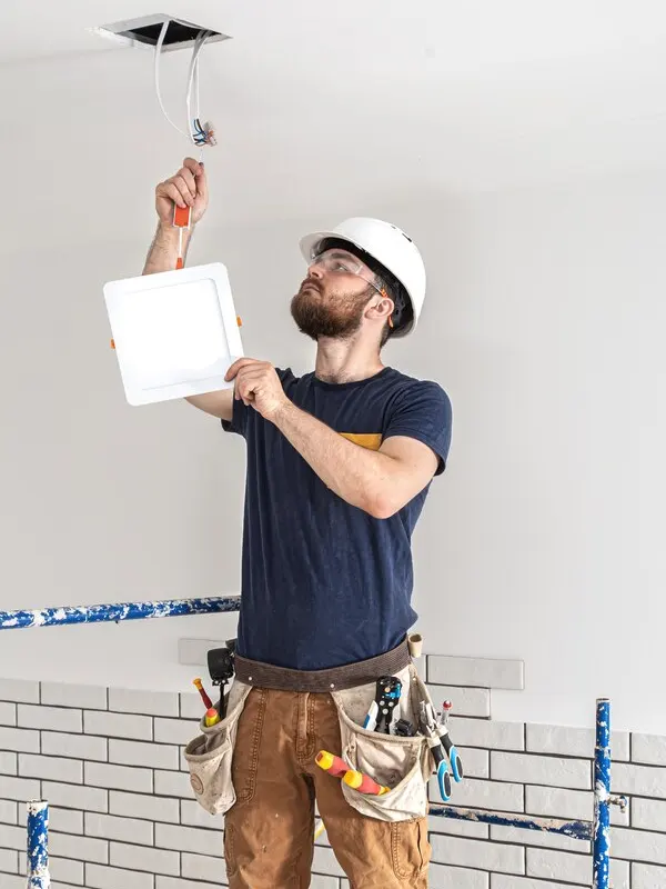 An emergency electrician in Jersey repairing a ceiling light fixture, responding to urgent electrical issues.