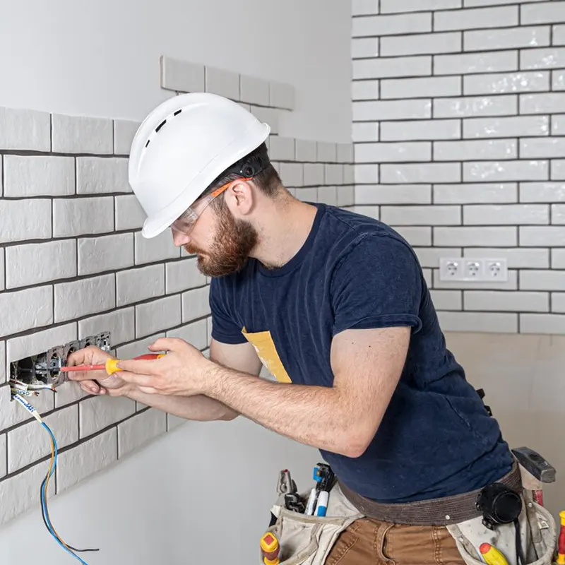 A professional electrician working on an electrical socket installation in a tiled kitchen wall in Jersey