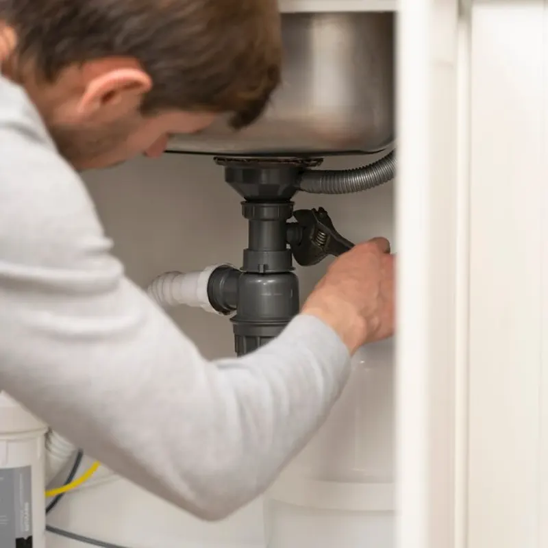 A local plumber tightening a pipe under the sink to fix a leak in Jersey.